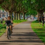 A woman cycling through a tree-lined path in Bordeaux, France on a sunny day.